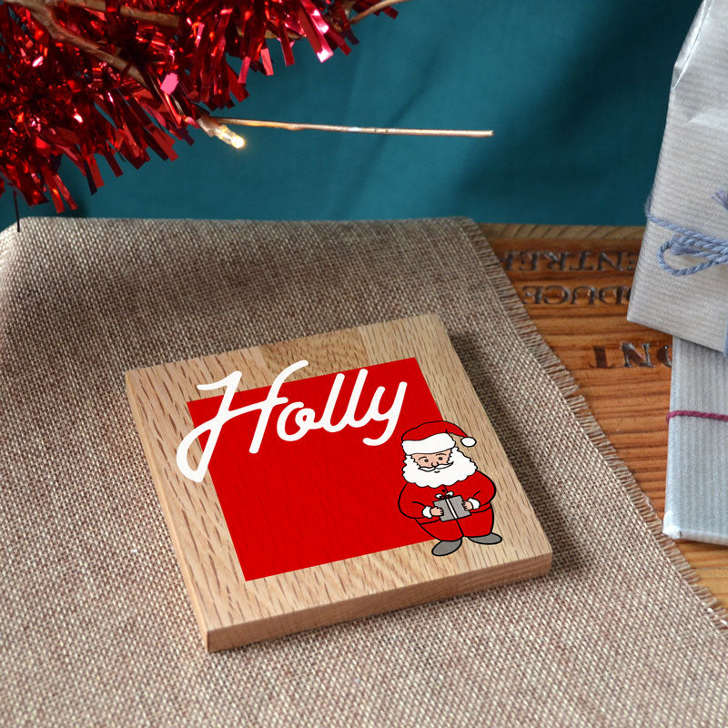 A personalised Christmas coaster in solid oak with a name and Santa printed on the front.