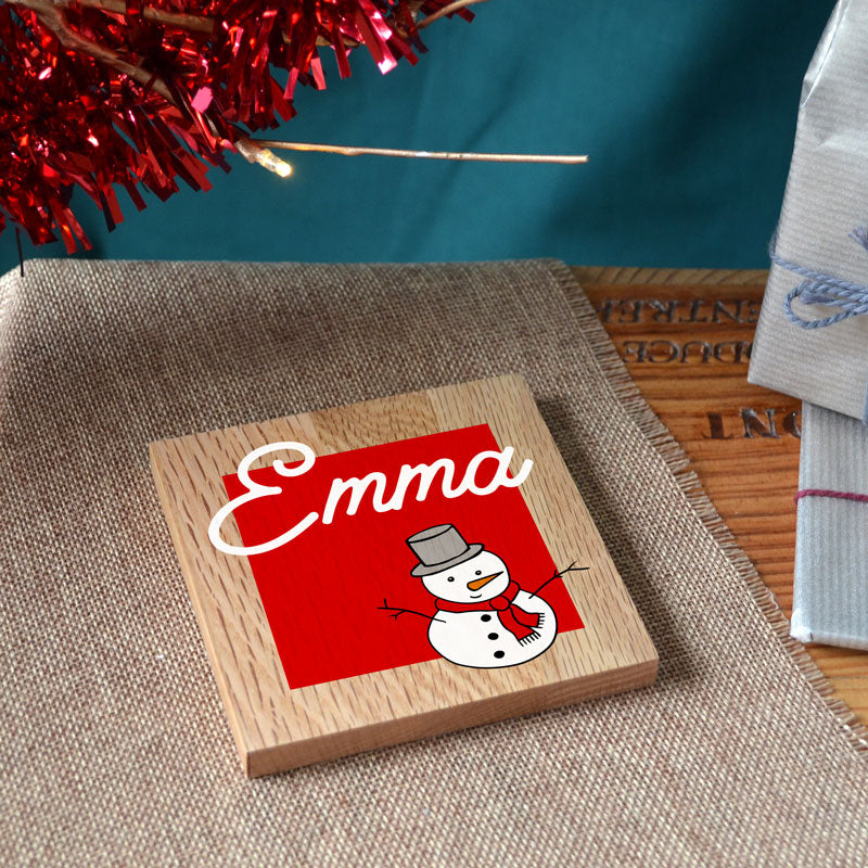 A personalised Christmas coaster in solid oak with a name and a snowman printed on the front.