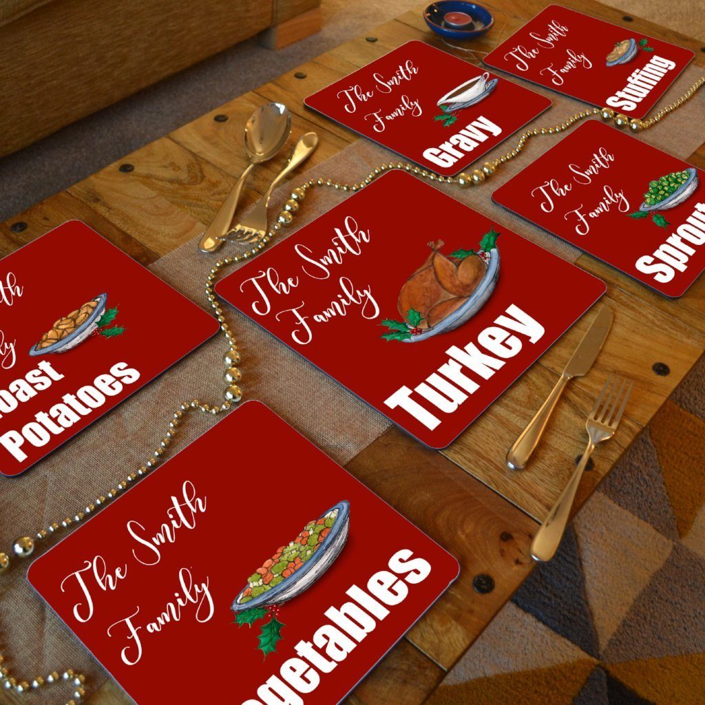 A dining table with personalised Christmas placemats on. The placemats are red with white text and illustrations of Christmas food 