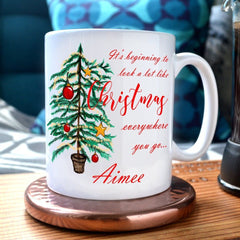 A personalised mug with the words "It's beginning to look a lot like Christmas" printed on in a red italic font.  The mug also has an illustration of a Christmas tree and the name "Aimee" printed on it 