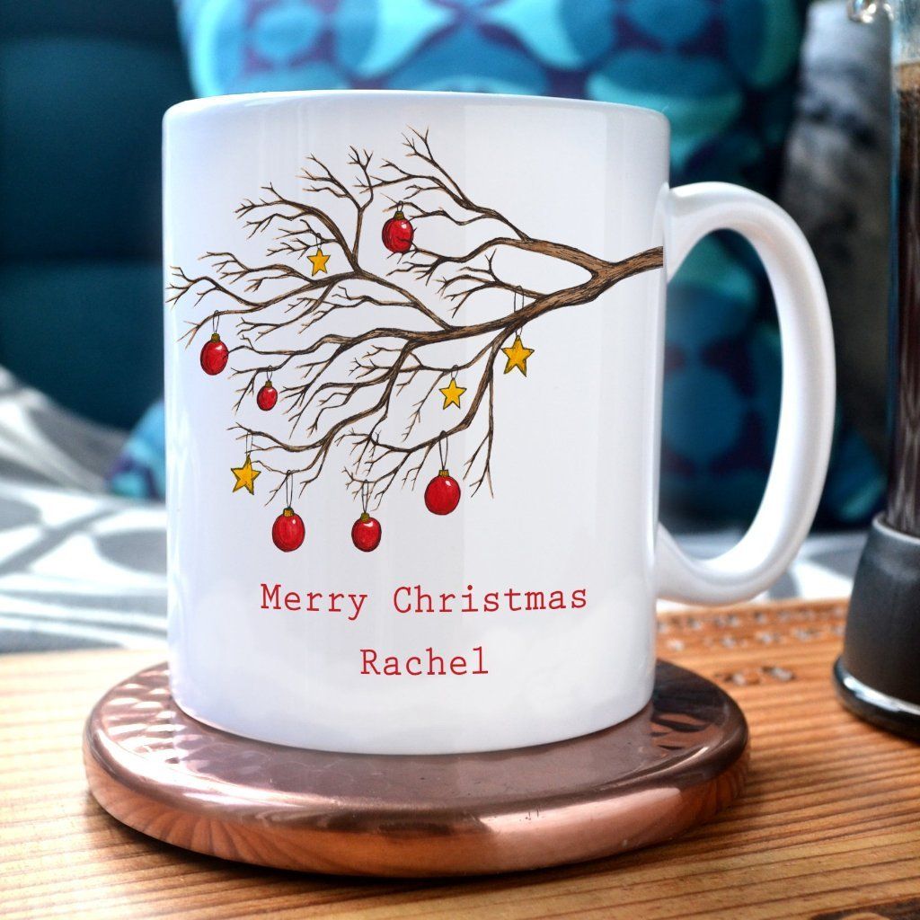 A personalised Christmas mug with a winter tree decorated with red baubles and gold stars. The mug has the message "Merry Christmas Rachel" printed onto it