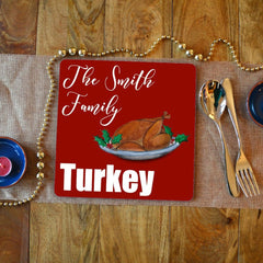 A personalised Christmas placemat with a turkey illustration. the placemat has a red background with white text reading "the Smith family turkey" 